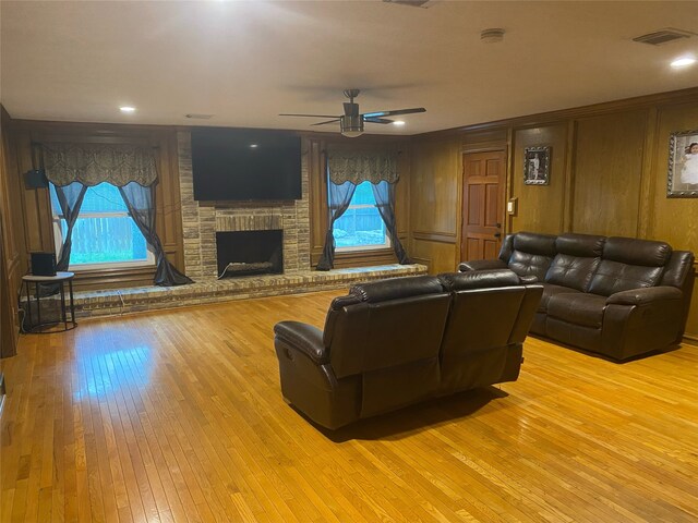 living room with ceiling fan, wood-type flooring, a brick fireplace, and wood walls