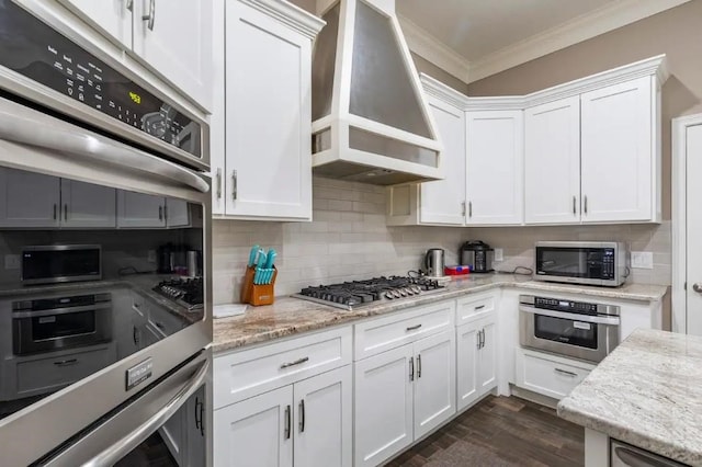 kitchen featuring stainless steel appliances, white cabinets, custom range hood, backsplash, and crown molding