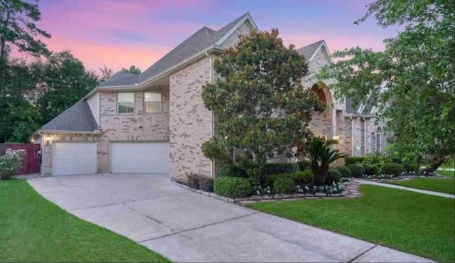 view of front of property with a yard, brick siding, an attached garage, and driveway