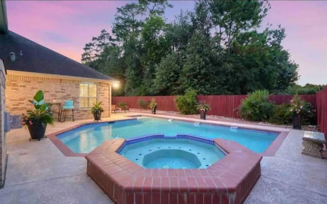 pool at dusk featuring a patio, a fenced backyard, and a pool with connected hot tub