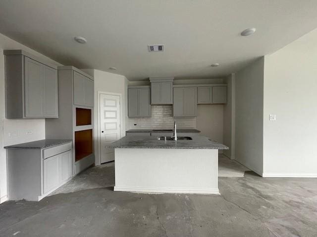 kitchen with gray cabinets, sink, an island with sink, and tasteful backsplash