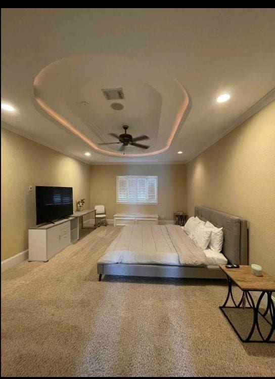 bedroom with ceiling fan, light carpet, and a tray ceiling