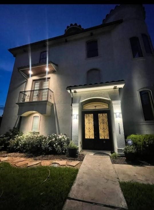 exterior entry at night with a balcony and french doors