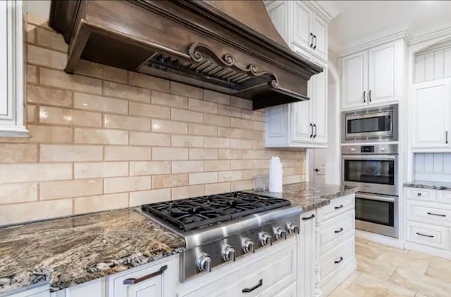 kitchen featuring custom exhaust hood, stainless steel appliances, backsplash, stone countertops, and white cabinetry