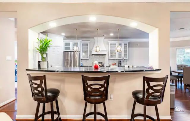 kitchen featuring custom range hood, stainless steel fridge, white cabinets, and a kitchen bar