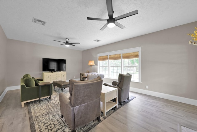 living room featuring wood-type flooring, a textured ceiling, and ceiling fan