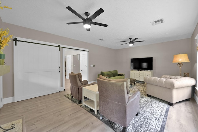 living room featuring a textured ceiling, a barn door, light hardwood / wood-style flooring, and ceiling fan