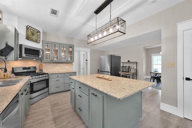 kitchen featuring a center island, light stone counters, light hardwood / wood-style floors, pendant lighting, and appliances with stainless steel finishes