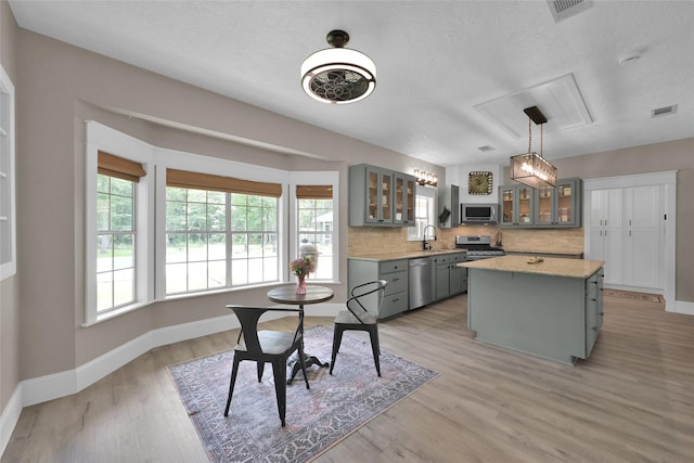 kitchen featuring light hardwood / wood-style floors, tasteful backsplash, decorative light fixtures, a kitchen island, and stainless steel appliances