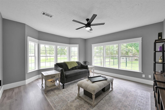 living room featuring a textured ceiling, light hardwood / wood-style flooring, and ceiling fan