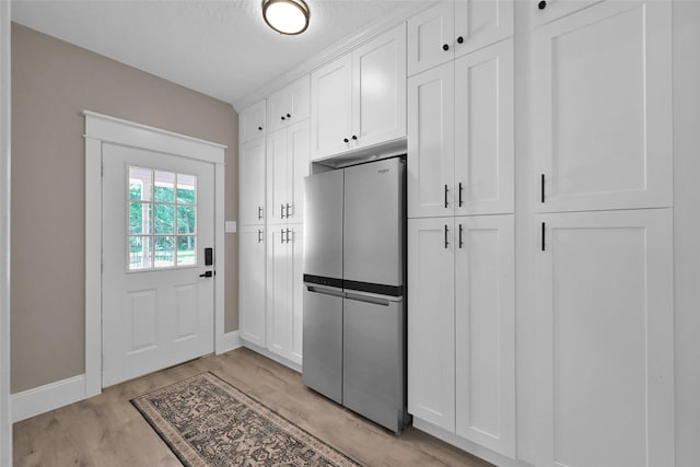 interior space featuring stainless steel refrigerator, white cabinets, light hardwood / wood-style floors, and a textured ceiling