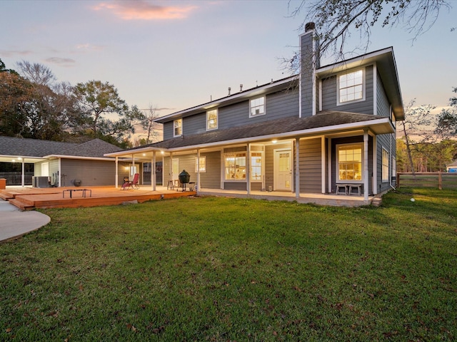 back house at dusk featuring central air condition unit, a deck, and a lawn