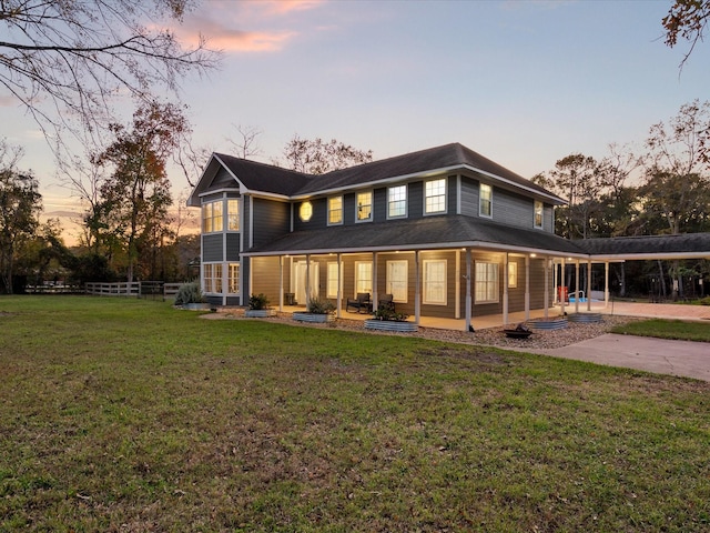 back house at dusk featuring a lawn and a carport