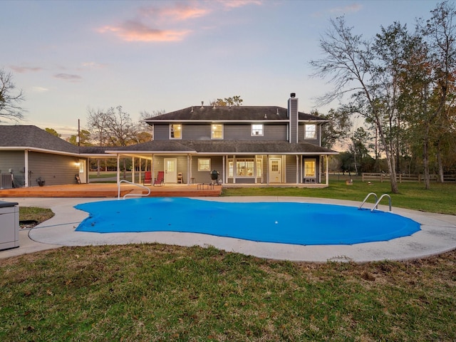 pool at dusk with cooling unit, a patio area, and a yard