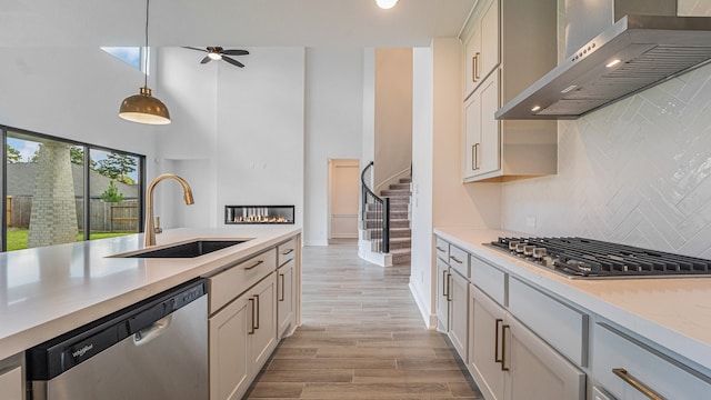 kitchen with appliances with stainless steel finishes, sink, backsplash, wall chimney exhaust hood, and pendant lighting