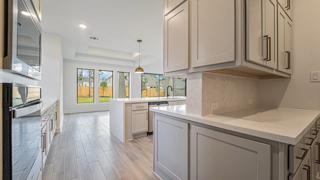 kitchen with light stone counters, appliances with stainless steel finishes, light wood-type flooring, sink, and decorative light fixtures