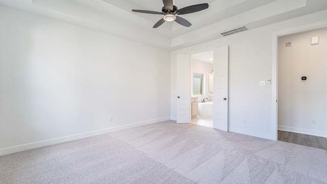 unfurnished bedroom with ensuite bathroom, light colored carpet, a tray ceiling, and ceiling fan