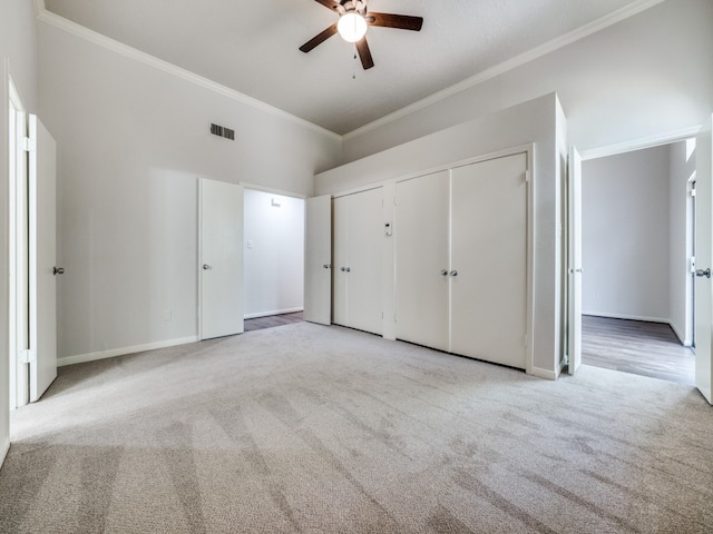 unfurnished bedroom with crown molding, light colored carpet, multiple closets, and ceiling fan