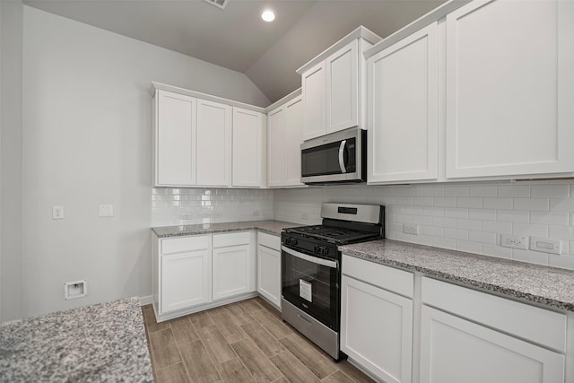 kitchen featuring appliances with stainless steel finishes, white cabinetry, decorative backsplash, vaulted ceiling, and light stone counters