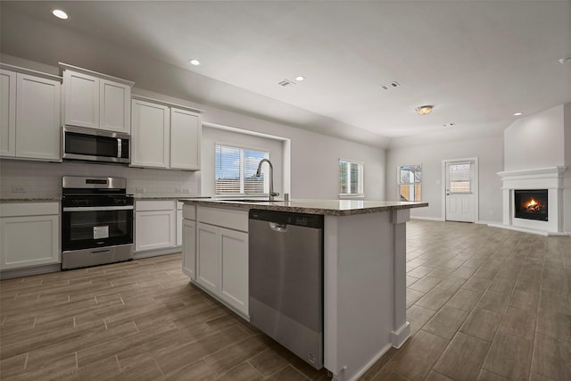 kitchen with sink, white cabinetry, appliances with stainless steel finishes, and a center island with sink