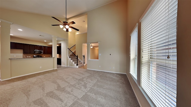 unfurnished living room featuring decorative columns, high vaulted ceiling, ceiling fan, and light colored carpet