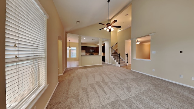 unfurnished living room with ornate columns, ceiling fan, high vaulted ceiling, and light colored carpet