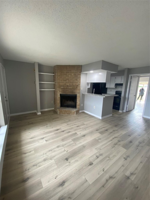 unfurnished living room with light wood-type flooring, a textured ceiling, and a brick fireplace