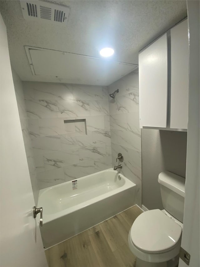 bathroom featuring hardwood / wood-style floors, tiled shower / bath combo, a textured ceiling, and toilet