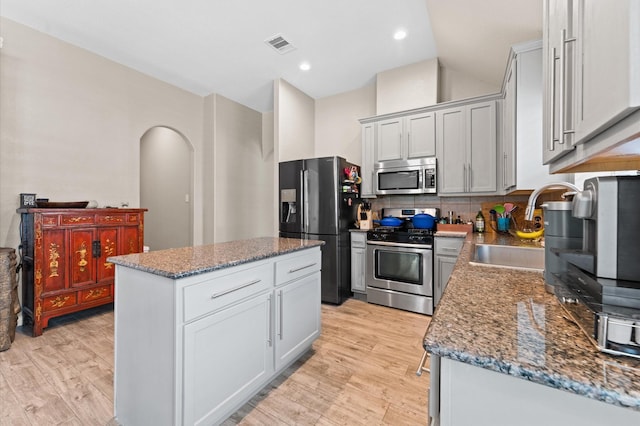 kitchen featuring decorative backsplash, appliances with stainless steel finishes, sink, dark stone countertops, and a kitchen island