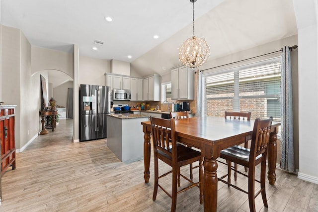 dining space with a notable chandelier, sink, vaulted ceiling, and light wood-type flooring