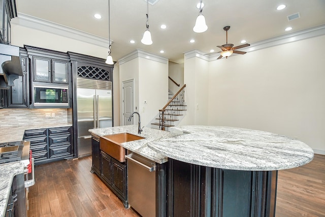 kitchen with backsplash, built in appliances, sink, and an island with sink