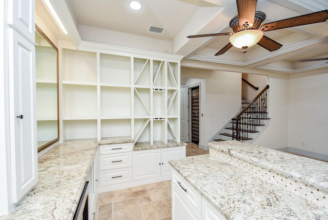 interior space with ceiling fan, white cabinetry, light stone countertops, and ornamental molding