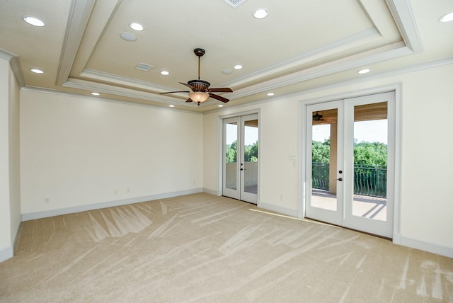 spare room with a tray ceiling, french doors, and light colored carpet