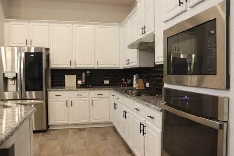 kitchen featuring light stone countertops, tasteful backsplash, stainless steel appliances, white cabinets, and light hardwood / wood-style floors