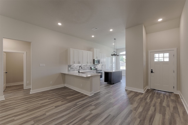 kitchen with pendant lighting, kitchen peninsula, sink, appliances with stainless steel finishes, and white cabinetry