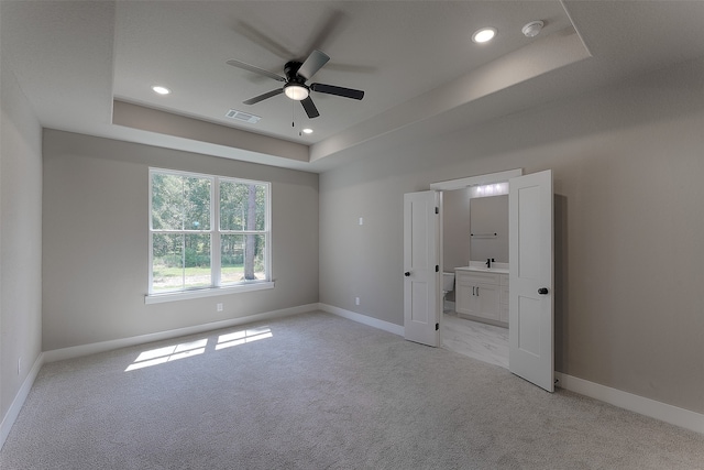 unfurnished bedroom featuring a tray ceiling, ceiling fan, and light colored carpet