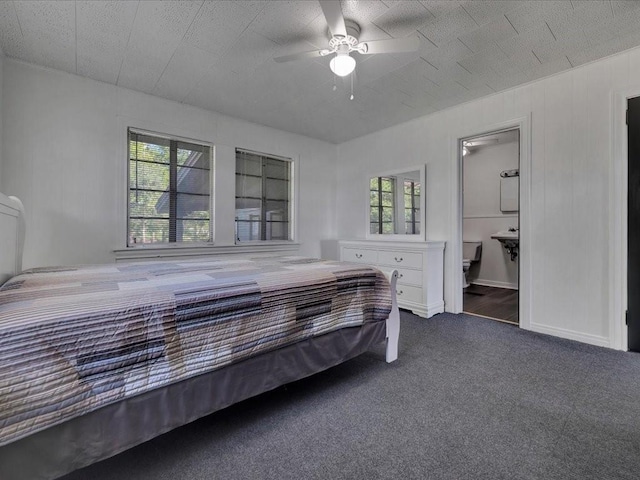 bedroom with ceiling fan, ensuite bathroom, dark carpet, and multiple windows