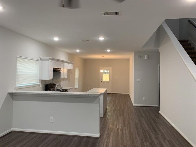 kitchen with backsplash, dark wood-type flooring, kitchen peninsula, a notable chandelier, and white cabinetry