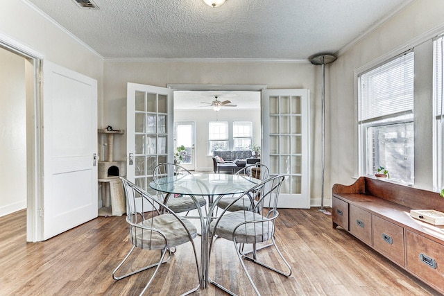 dining room with ceiling fan, french doors, light hardwood / wood-style flooring, a textured ceiling, and ornamental molding