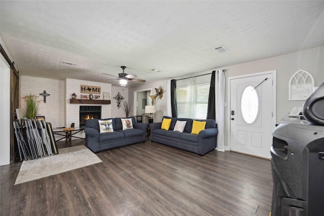 living room featuring ceiling fan, dark wood-type flooring, a barn door, a textured ceiling, and a fireplace