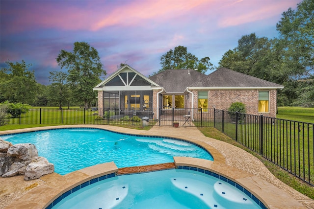 pool at dusk featuring a lawn, a patio area, and an in ground hot tub