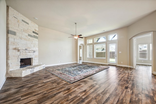 unfurnished living room featuring a stone fireplace, dark hardwood / wood-style floors, and ceiling fan