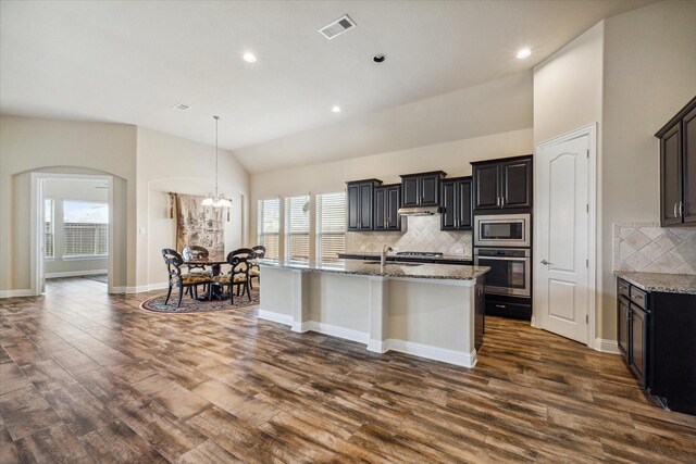 kitchen with stainless steel appliances, tasteful backsplash, an island with sink, dark wood-type flooring, and lofted ceiling