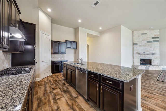 kitchen with a fireplace, a center island with sink, appliances with stainless steel finishes, dark hardwood / wood-style floors, and tasteful backsplash