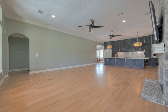 unfurnished living room with a textured ceiling, a fireplace, light wood-type flooring, sink, and ceiling fan