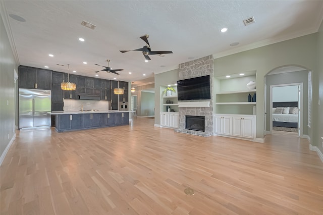 unfurnished living room with light hardwood / wood-style floors, a fireplace, built in features, ceiling fan, and a textured ceiling