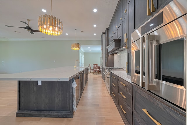 kitchen with light hardwood / wood-style flooring, ceiling fan with notable chandelier, a large island with sink, ornamental molding, and pendant lighting