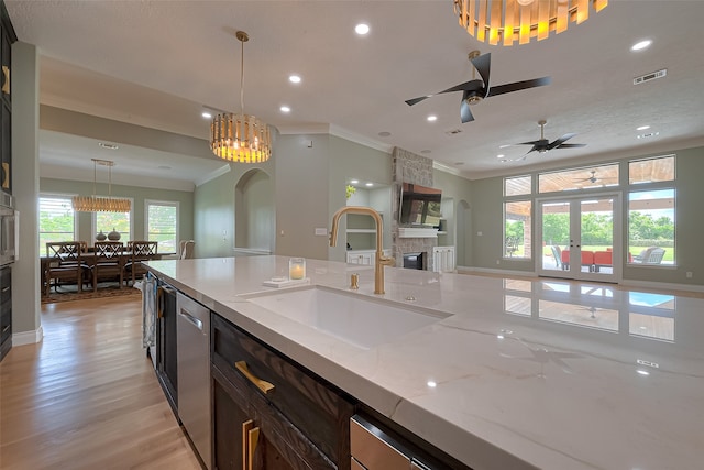 kitchen featuring light hardwood / wood-style floors, a fireplace, ceiling fan with notable chandelier, light stone countertops, and sink