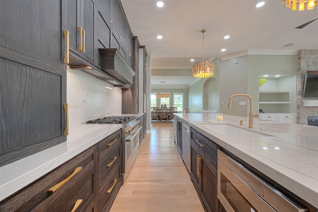 kitchen with decorative light fixtures, stainless steel appliances, ornamental molding, light wood-type flooring, and sink