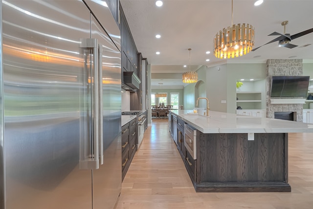 kitchen featuring light hardwood / wood-style floors, a fireplace, stainless steel built in fridge, a center island with sink, and dark brown cabinets